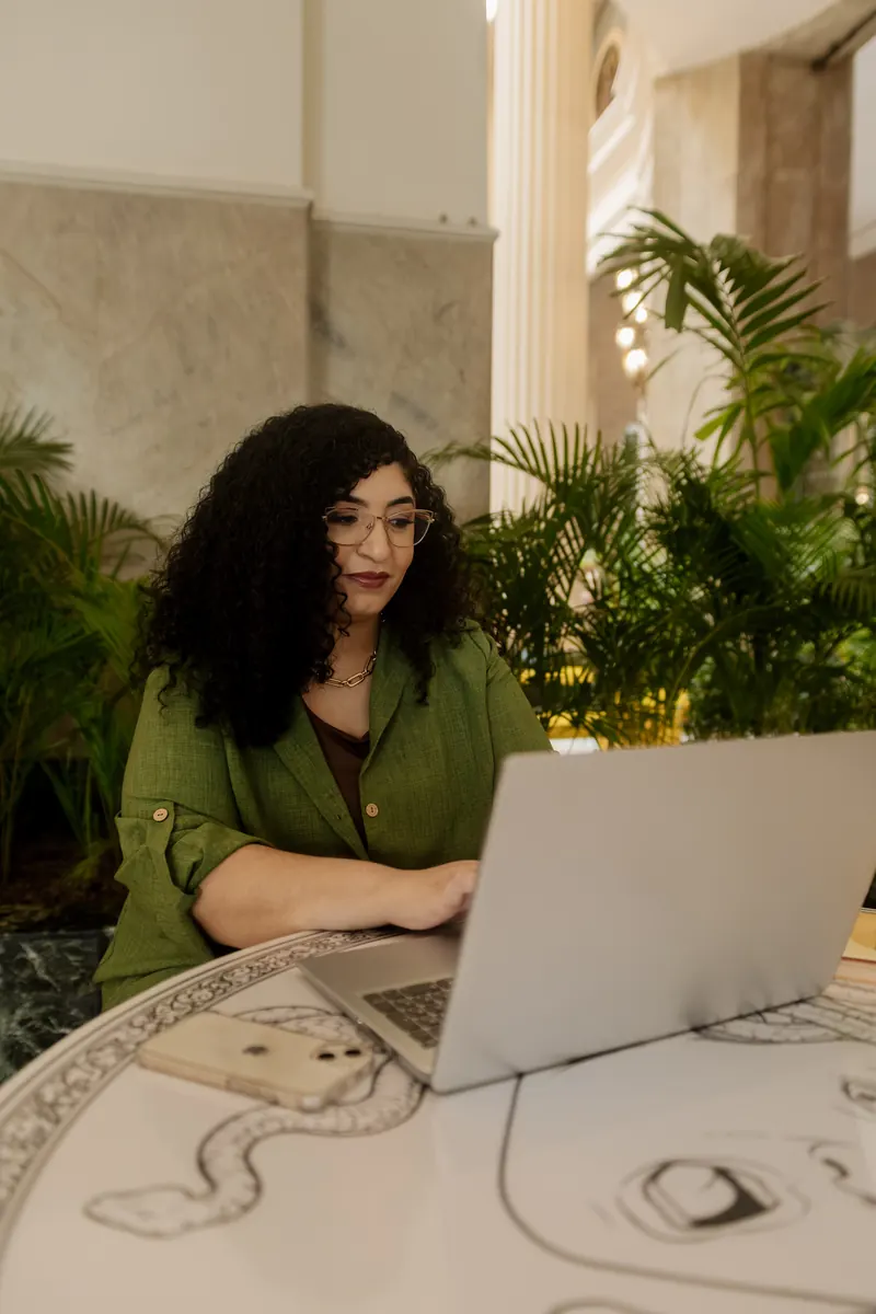Camyla em atendimento online, digitando no notebook em um ambiente com plantas